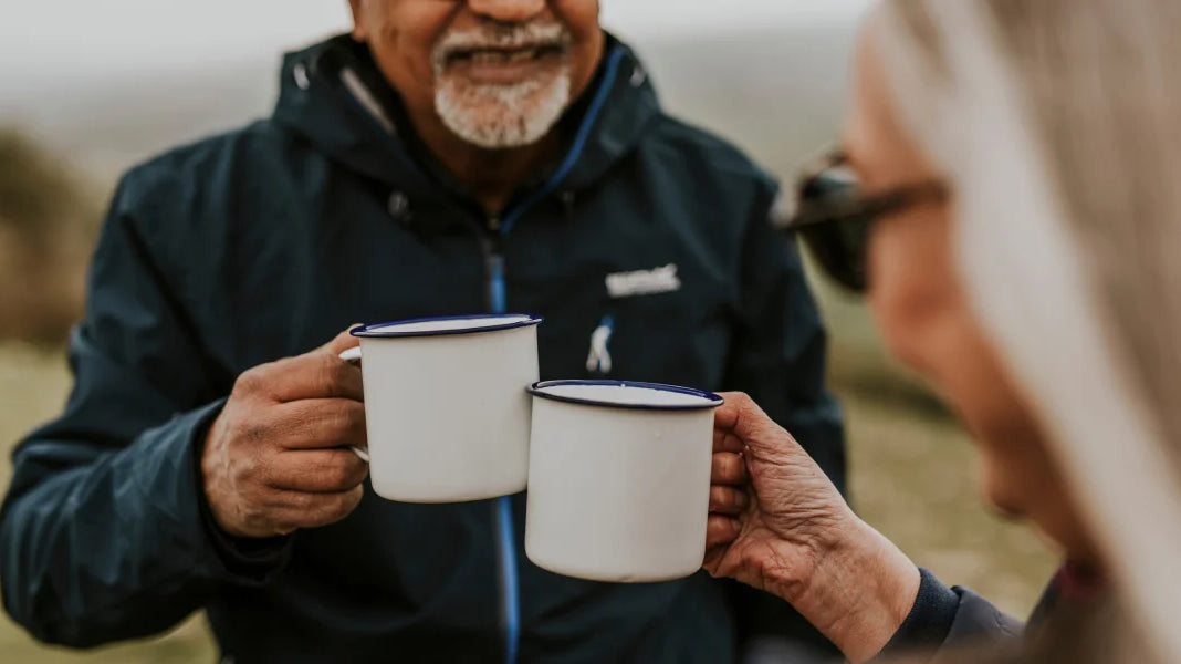 Un couple âgé trinquant avec des tasses de café instantané, partageant un moment de convivialité et de complicité.