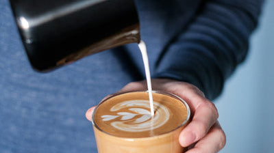 Flatwhite en préparation dans une tasse en verre avec un pichet de café noir