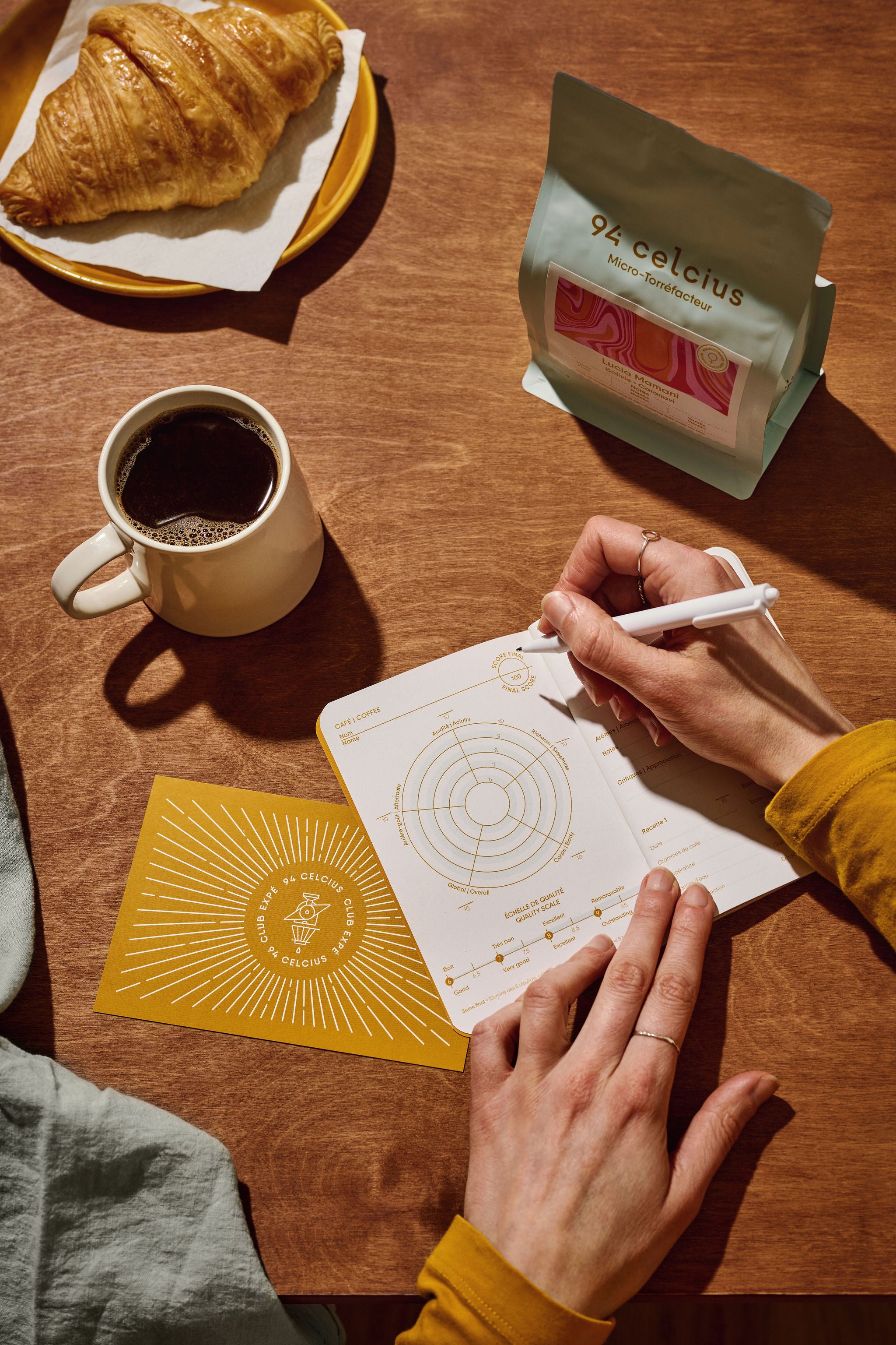 Abonnement de café le club expé, prise de note de dégustation et croissant sur une table en bois.
