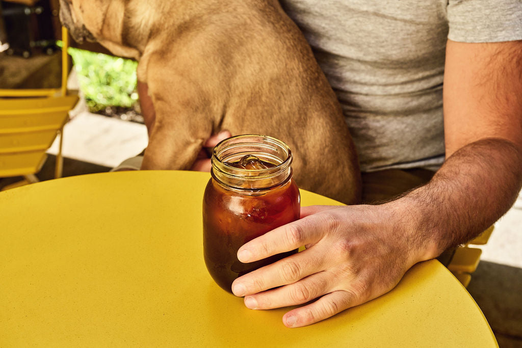 Homme en train de boire un café de spécialité assis sur une table jaune avec un chien