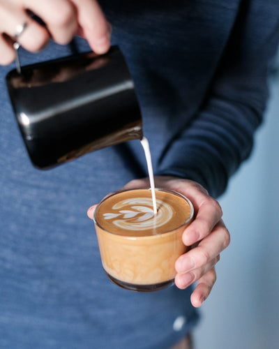 Flatwhite en préparation dans une tasse en verre avec un pichet de café noir