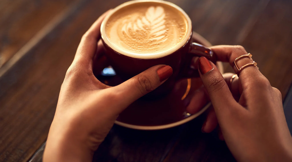 Une femme tenant une tasse de café sur une table en bois, illustrant l'achat de café.