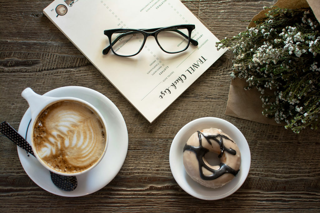 Cappucino sur une table avec un beigne et des lunettes